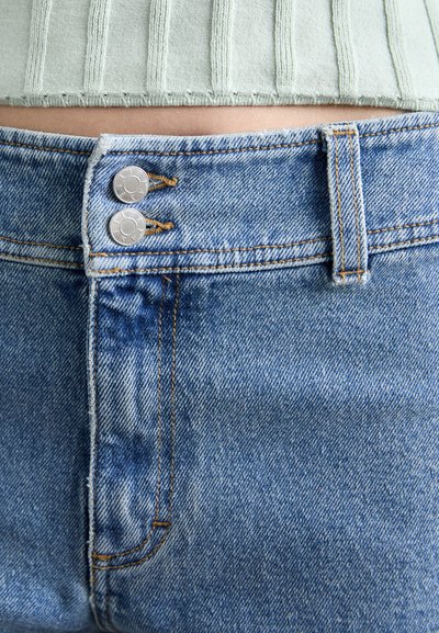 Heledad sinine teksariided, millel on kaks hõbedast nööpi ja kontrastne oranž õmblus. Kanga tekstuur on pehme ja veidi tuhm.