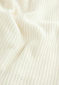 Gros plan d'un tissu blanc doux à texture gaufrée, avec des plis et des ombres délicats.
