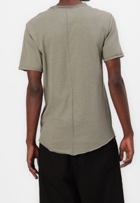 Olijfgroene korte mouw blouse met een rechte snit, zichtbare naad aan de achterkant, onafgewerkte randen en een gebogen zoom. Zachte, gestructureerde stof.