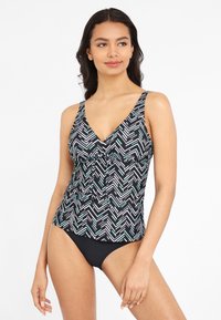 Zwart-witte tankini top met geometrisch patroon, voorzien van een V-hals, verstelbare bandjes en een geplooid detail aan de voorkant. Gecombineerd met zwarte bikinibroekjes.