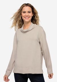 Sudadera beige con cuello de cowl, hecha de un tejido suave, con mangas largas y un ajuste relajado, que presenta un dobladillo inferior recto y costuras mínimas.