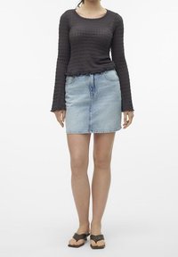 Černý top s dlouhým rukávem a texturou, s volánkovými okraji, spárovaný s světle modrou džínsovou minisukní a černými sandály na klínu.