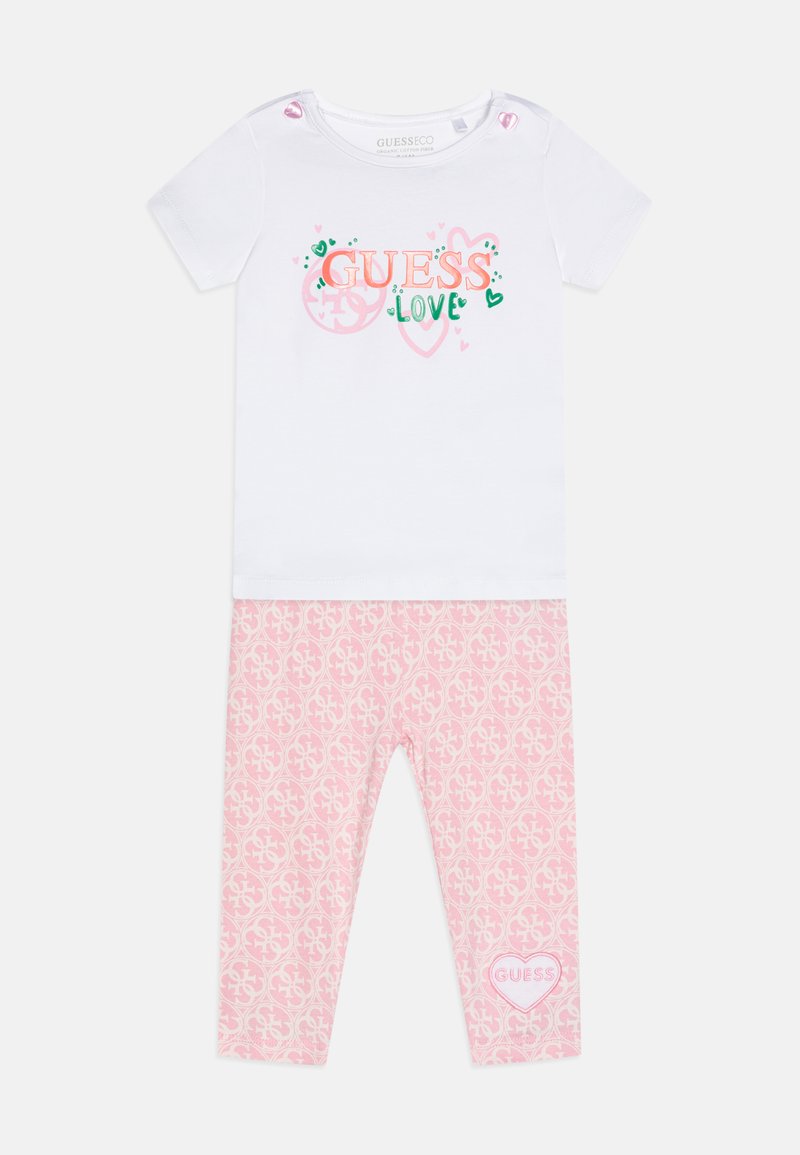 Fehér, rövid ujjú póló "GUESS LOVE" grafikával, rózsaszín leggings-szel párosítva, amely ismétlődő logómintát és szív részletet tartalmaz.