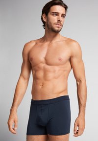 Boxers-briefs pour homme en bleu marine, fabriqués en tissu doux, avec un design ajusté, une taille élastique et des coutures décoratives à l'avant.