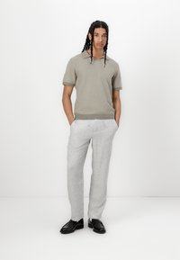 Polo de malha cinza claro com mangas curtas, combinado com calças texturizadas cinza claras e mocassins pretos. Design simples e limpo.