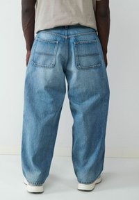 Jeans de mezclilla azul claro con un corte holgado, dos bolsillos traseros y un diseño de pierna recta. Presenta una costura típica a lo largo de las costuras.