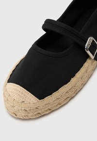 Fekete vászontalpú espadrilles, kerek orral, juta talppal és az elején csattal. Krémszínű szőtt orrborítása van.