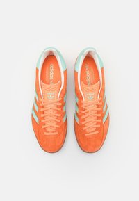 Pair of Adidas sneakers in bright orange suede with light blue stripes and heels, viewed from above against a white background.
