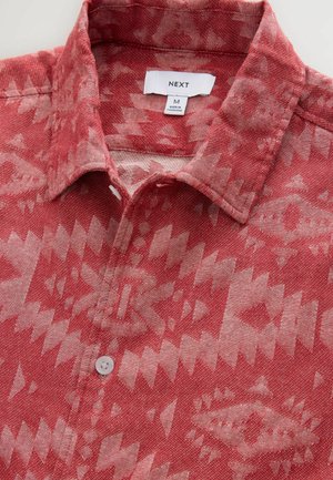 Chemise à motifs rouges avec col, patte de boutonnage, et un design géométrique dans des teintes plus claires de rouge et de beige. Fabriquée en tissu respirant.