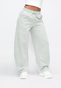 Lysegrå joggingbukser med elastisk talje og snøre. Har vide ben og lommer, lavet af et blødt, tekstureret stof.