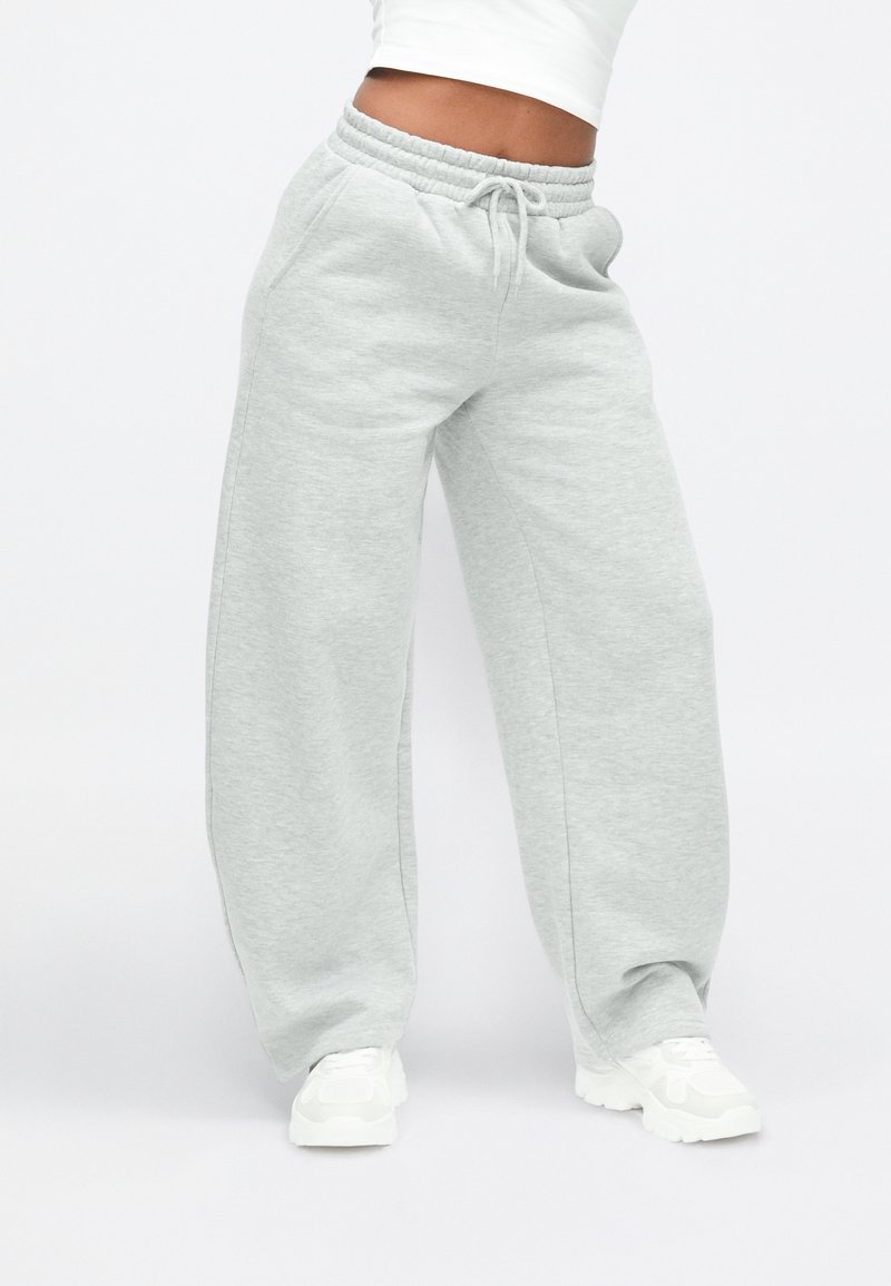 Lysegrå joggingbukser med elastisk talje og snøre. Har vide ben og lommer, lavet af et blødt, tekstureret stof.
