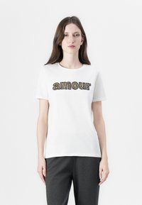 White short-sleeve t-shirt with "amour" printed in leopard pattern font across the chest, paired with dark gray pants. Smooth fabric texture.