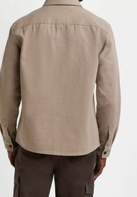 Beżowa koszula z długim rękawem, kołnierzykiem, mankietami zapinanymi na guziki oraz prostym dołem, wykonana z teksturowanej tkaniny. Charakteryzuje się minimalistycznym wzornictwem bez wzorów.
