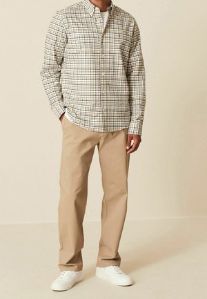 Camicia button-up beige con un motivo a quadri multicolore, abbinata a pantaloni beige chiaro e sneakers bianche, che mostrano un look informale.