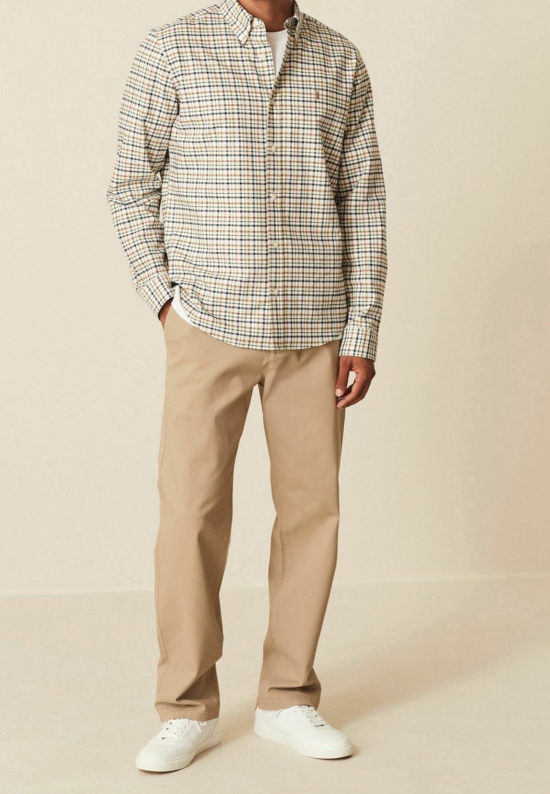 Beige overhemd met een meerkleurig geruit patroon, gecombineerd met lichtbeige broeken en witte sneakers, wat een casual uitstraling creëert.