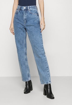 Jeans taille haute bleu clair, à coupe ample, fabriqués en denim avec des coutures visibles. Comprend cinq poches et des boutons en métal.