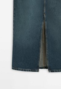 Jupe en denim bleu foncé avec une fente au centre du dos montrant les détails des coutures intérieures et une surpiqûre orange sur fond blanc.