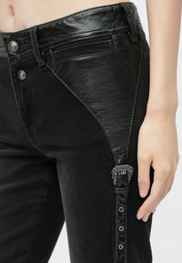 Μαύρα τζιν με υβριδικό ύφασμα από τεχνητό δέρμα στο γοφό, ασημί μεταλλικές λεπτομέρειες και κουμπιά με κλείσιμο τύπου snap στη πλευρά.