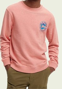 Ljust rosa sweatshirt i mjukt material, med rund halsringning och en grafisk logotyp på bröstet med palmträd och textdetaljer.