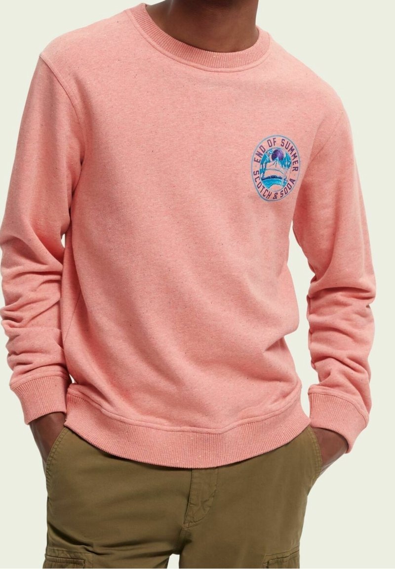 Ljust rosa sweatshirt i mjukt material, med rund halsringning och en grafisk logotyp på bröstet med palmträd och textdetaljer.