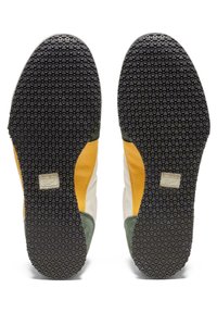 Sula av skor med en strukturerad svart gummiyta, med gröna, gula och vita läderdetaljer samt en silverfärgad logotyp.