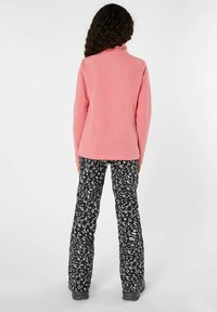 Sudadera de forro polar en color rosa con un cuello alto, combinada con pantalones negros con un patrón floral blanco, diseñada para la comodidad y la movilidad.