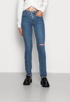 Jeans skinny em denim azul claro com um joelho desgastado. Combinados com um top cropped branco e sapatos de plataforma pretos. Textura suave, design justo.