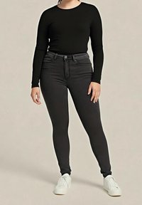 Osoba ubrana w czarną bluzkę z długim rękawem, czarne obcisłe jeansy z wysokim stanem i białe trampki, stojąca na jednolitym tle.