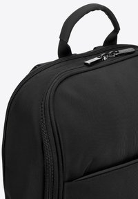 Zaino in nylon nero con manico superiore, zip liscia e superficie testurizzata con tasca frontale. Design compatto con accenti minimi.