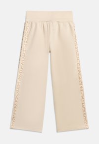 Μπεζ παντελόνια με φαρδιά μπατζάκια, ελαστική μέση και ανοιχτό καφέ ρίγες με μοτίβο λεοπάρ που τρέχουν κατά μήκος των εξωτερικών πλευρών κάθε μπατζακιού.