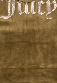 Tessuto verde oliva con una morbida textura, adornato con la scritta "Juicy" in strass luccicanti nella parte superiore, che presenta un design del carattere curvo.
