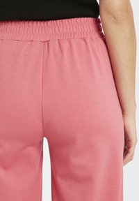 Ljusrosa byxor med elastisk midja och en slät textur. Designen har en avslappnad passform och är minimalistisk utan framträdande mönster eller detaljer.