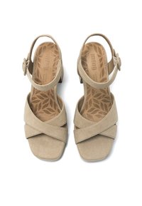 Sandalias de ante beige con tiras cruzadas, cinta en el tobillo y un tacón pequeño. La plantilla texturizada presenta un patrón de hojas. Diseño de punta cuadrada.