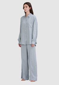 Jasnoniebieska, długorękawowa koszula z guzikami z kieszonką, w zestawie z dopasowanymi szerokimi spodniami; miękki materiał, luźny krój.