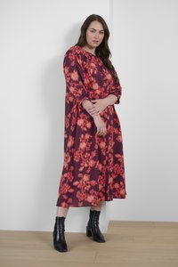 Robe longue à boutons en tissu bordeaux avec un motif floral en orange vif. Comprend des manches longues et est associée à des bottines noires.
