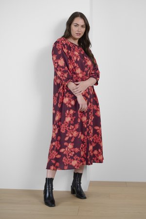 Long, button-up dress in a burgundy fabric with a floral pattern in bright orange. Includes long sleeves and is paired with black ankle boots.