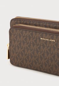 Brown Michael Kors wallet featuring a textured monogram pattern, two zippered compartments, and gold-tone hardware with a logo detail.