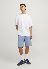 Fehér, túlméretezett póló, világoskék farmer rövidnadrág, fehér zokni és sötétkék sportcipő. Egyszerű, hétköznapi dizájn, laza szabással.