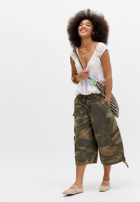 Λευκό ελαφρύ μπλουζάκι με λεπτομέρειες βολάν, συνδυασμένο με χακί cargo σορτς καμουφλάζ. Διαθέτει ριγέ τσάντα χειρός με μπλε ανθισμένη λεπτομέρεια και μπεζ φλατ παπούτσια.