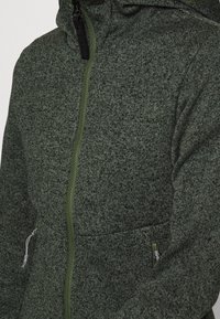 Grüner, strukturierter Kapuzenpullover mit Reißverschluss aus einem gestrickten Material. Verfügt über einen hohen Kragen, einen kontrastierenden Reißverschluss und zwei Seitentaschen.