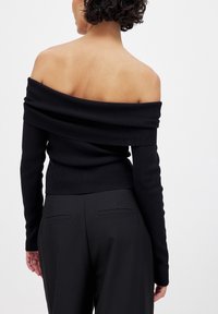 Zwart geribbelde gebreide trui met een off-shoulder ontwerp, lange mouwen en een aansluitend silhouet, gecombineerd met op maat gemaakte zwarte broek.