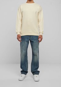 Felpa color crema con vestibilità rilassata, polsini e scollo a costine abbinata a jeans a gamba dritta azzurri sbiaditi e sneakers bianche.