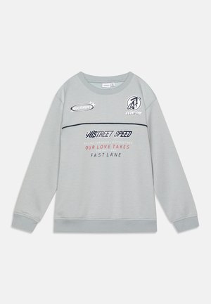 Svetlošedý mikina s okrúhlym výstrihom, zdobená rôznymi potlačami log a textov v kontrastných farbách, vrátane námorníckej a červenej.