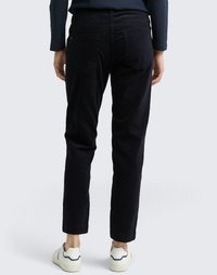 Pantalon en velours côtelé bleu foncé à jambe droite, avec poches arrières visibles et coupe ajustée, associé à des baskets blanches.