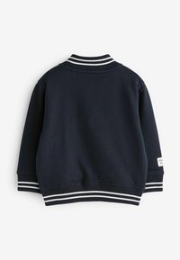 Sudadera azul marino con cuello y puños acanalados, que presenta franjas blancas. Tejido simple y texturizado con corte recto y sin cierres visibles.