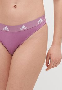 Fialové bavlněné tanga s měkkým elastickým pasem a bílým logem Adidas. Hladká textura a design s minimálním krytím.