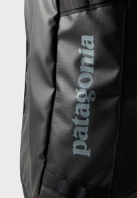 Černá voděodolná taška s texturovaným povrchem a šedým logem "patagonia". Obsahuje nastavitelné popruhy a robustní konstrukci.