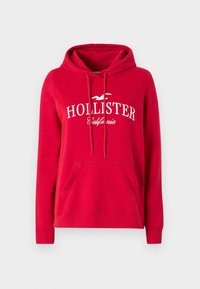 Sudadera roja hecha de una mezcla de algodón con un bolsillo tipo canguro en la parte frontal. Presenta el texto y el logo en blanco "HOLLISTER" en el pecho. Capucha ajustable con cordón.