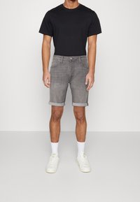 Szare spodenki dżinsowe z podwiniętymi mankietami, noszone z czarnym t-shirtem i białymi trampkami. Krótka długość, gładka tekstura, standardowy design z czterema kieszeniami.