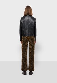 Black leather jacket with a straight cut, high collar, and long sleeves, paired with brown leopard print wide-legged pants and black shoes.